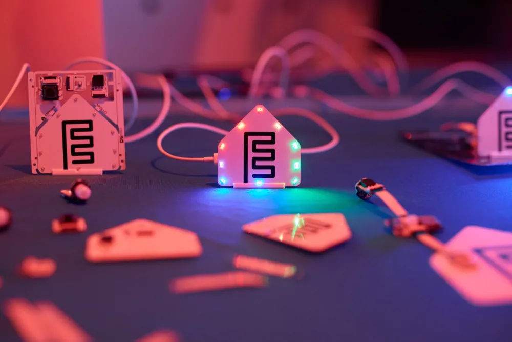 Kit ESPHome: Empieza Hoy 2 Módulos del Kit de Inicio ESPHome sobre una mesa, con el módulo de notificación en forma de logo de ESPHome iluminado por luces LED de colores.